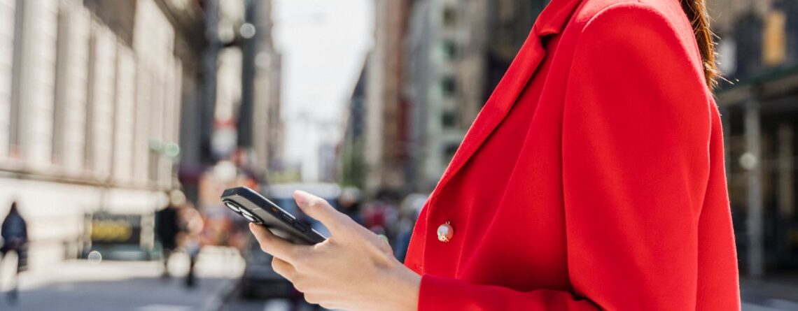 Kobieta na ulicy przegląda stronę internetową na telefonie trzymanym w dłoni