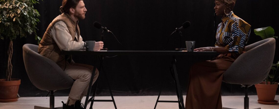 Dwie osoby nagrywające podcast przy stole z mikrofonami w studiu